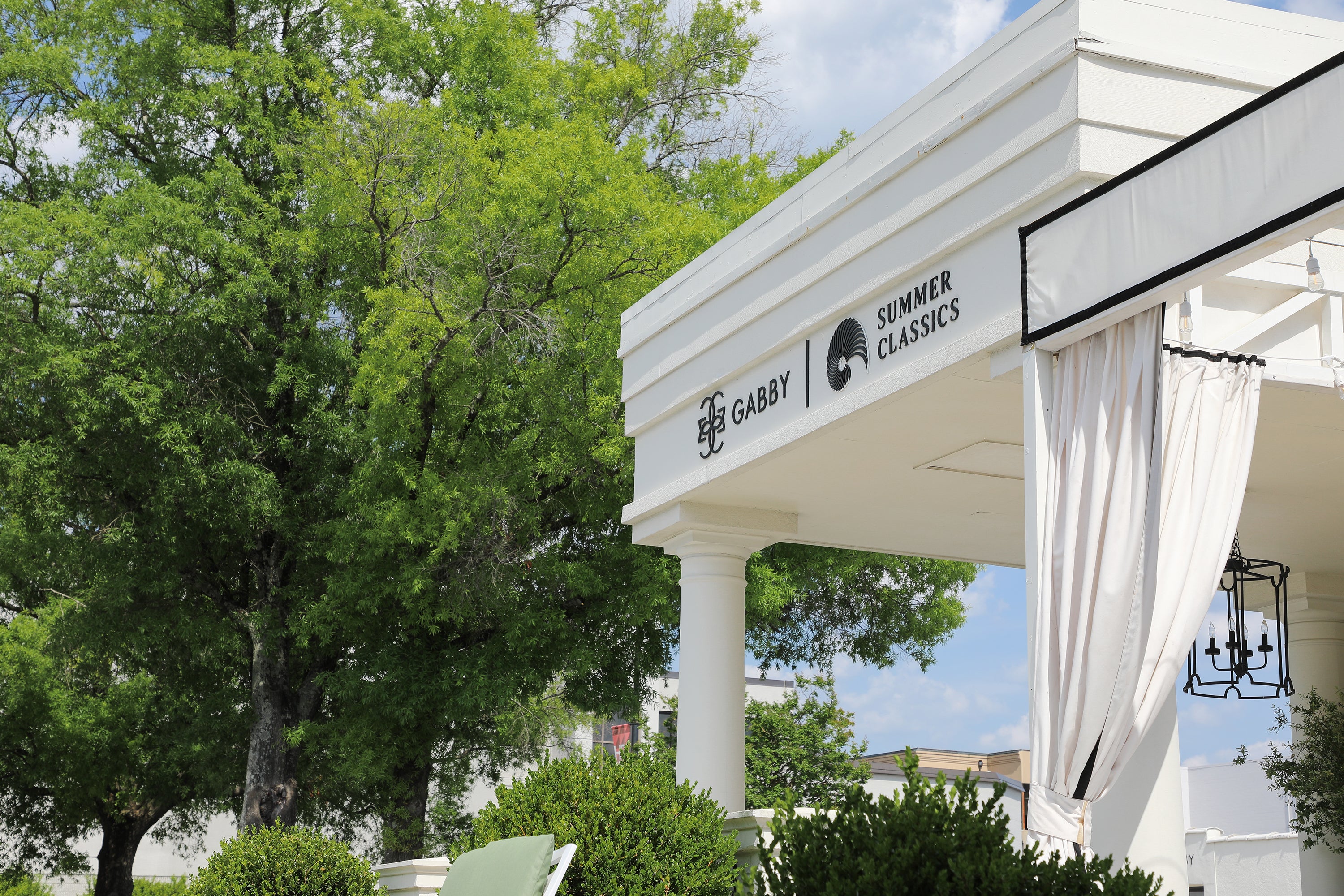 Gabby and Summer Classics branded showroom pavilion exterior at High Point Furniture Market Spring 2026, featuring white columned architecture, draped curtains, and lush green surroundings